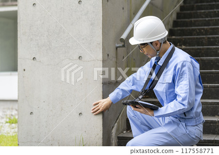 一名穿著工作服的男子正在檢查建築物的外牆 117558771