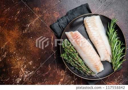 Raw cod loin fillet steaks with herbs on plate. Dark background. Top view. Copy space Raw cod loin fillet steaks with herbs on plate. Dark background. Top view. Copy space 117558842