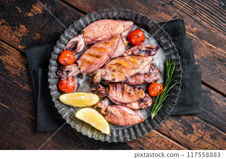 Grilled squid, calamary in a plate with herbs. Wooden background. Top view Grilled squid, calamary in a plate with herbs. Wooden background. Top view 117558883