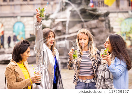 Friends enjoying drinks by a fountain, cherishing happy moments and socializing outdoors 117559167