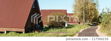 The concept of glamping and renting a chalet for weekend. Wooden house with a veranda in nature around coniferous trees The concept of glamping and renting a chalet for weekend. Wooden house with a veranda in nature around coniferous trees 117560216