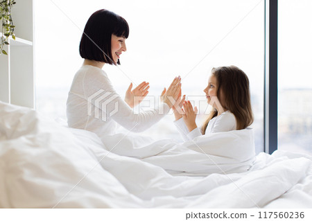 Mother and daughter playing clapping game in bed 117560236