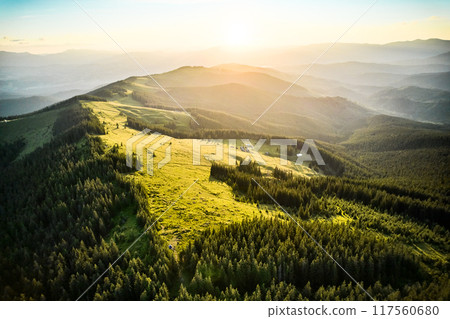 Breathtaking aerial view of mountain landscape at sunset. Golden light bathes rolling hills and lush forests, creating serene and idyllic scene. Distant mountains adding depth to picturesque vista. 117560680