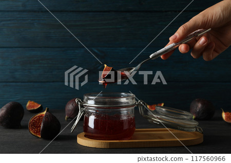 Glass jar with fig jam and spoon in hand, cut figs on wooden background Glass jar with fig jam and spoon in hand, cut figs on wooden background 117560966