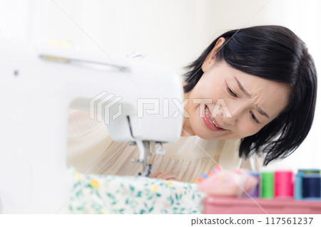 Hobby: Middle-aged woman sewing with a sewing machine Hobby: Middle-aged woman sewing with a sewing machine 117561237