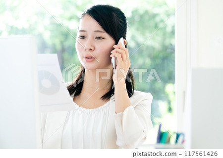 A woman talking on a smartphone with documents in her hands 117561426