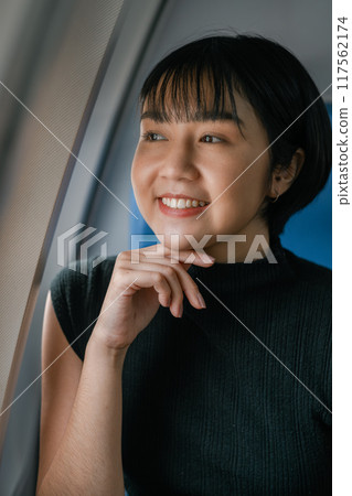 A cheerful woman with short hair smiling and looking out an airplane window, enjoying her travel experience. 117562174