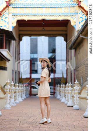 A woman in a yellow dress stands in front of a building with a gold 117562848