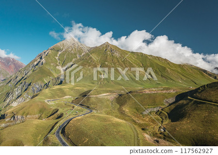 A Serene Mountain Landscape featuring a Winding Road that stretches under a Clear Blue Sky 117562927