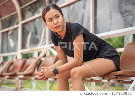 Tired female runner sitting down to take a break from her run at an outdoor running track 117563932