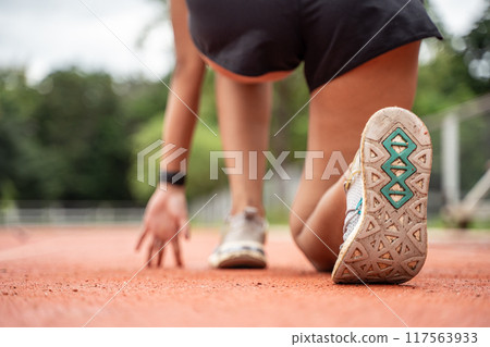Close up of a female runner shoe from behind while she crouching down in a starting position at the running track 117563933