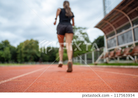 Back view and out of focus of a female runner running at an outdoor running track 117563934