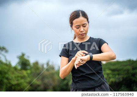 Young Asian female runner checing her run time on her smart watch after her run at an outdoor running track Young Asian female runner checing her run time on her smart watch after her run at an outdoor running track 117563940