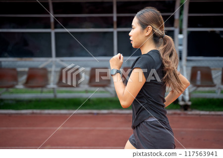 Side view of a young woman in black running clothes running during her evening exercise Side view of a young woman in black running clothes running during her evening exercise 117563941