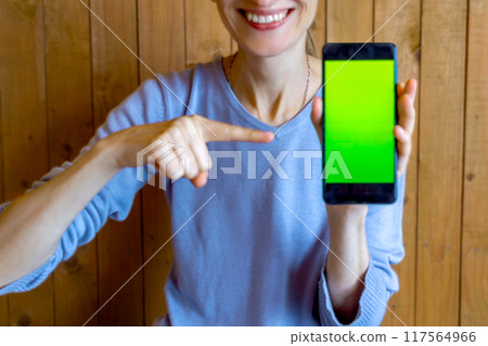 Smiling thin woman shows chromakey on smartphone screen. unrecognizable persona. Close-up. Soft focus, blurred 117564966
