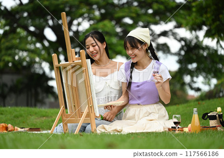 Two young asian women painting on easel with watercolors in a park Two young asian women painting on easel with watercolors in a park 117566186
