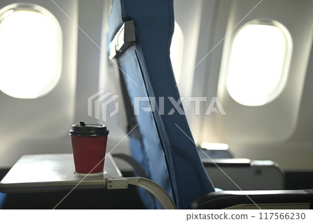 A red disposable coffee cup on airplane tray table in front of a blue chair A red disposable coffee cup on airplane tray table in front of a blue chair 117566230