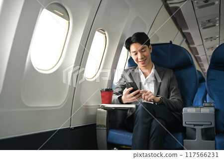 Successful asian businessman wearing suit using smartphone while sitting next to window in an airplane 117566231