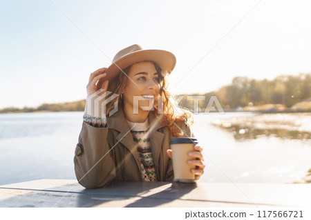 Fall concept woman drinking coffee on bench against backdrop of lake. Enjoying, solitude with nature Fall concept woman drinking coffee on bench against backdrop of lake. Enjoying, solitude with nature 117566721