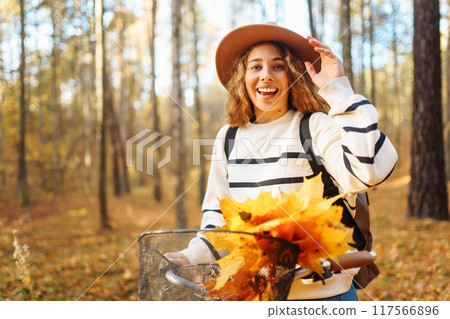 Happy woman with curly hair rides bicycle in sunny autumn park. Outdoor. Lifestyle. Nature concept. 117566896