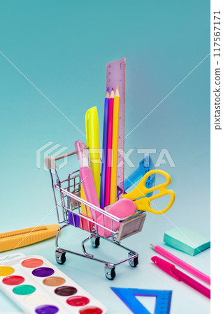 Shopping trolley with stationery items and school supplies on blue background. back to school and education background concept. Shopping cart, supermarket trolley with school supplies. Preparing for s Shopping trolley with stationery items and school supplies on blue background. back to school and education background concept. Shopping cart, supermarket trolley with school supplies. Preparing for s 117567171