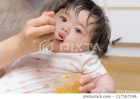 [Baby with tied hair eating baby food] 117567196