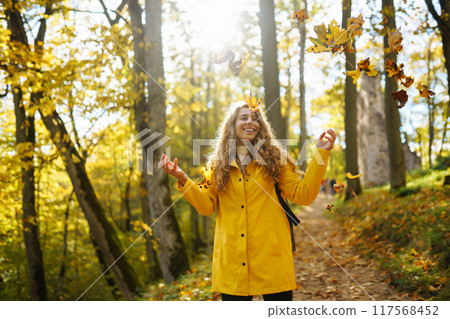 Woman in a yellow coat with backpack walks along wooden staircase, enjoying autumn scenery in forest 117568452