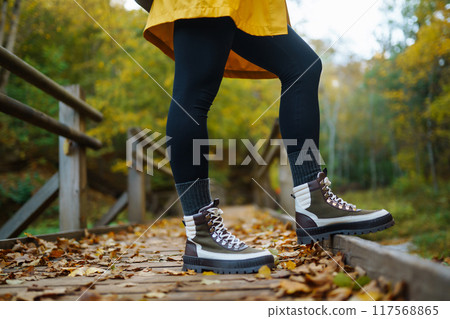 Women's feet in boots go along a wooden walking path in the autumn forest. 117568865