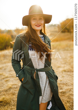 Beautiful stylish girl walks in the autumn park. The girl is dressed in a green coat and a red hat. Beautiful stylish girl walks in the autumn park. The girl is dressed in a green coat and a red hat. 117569370