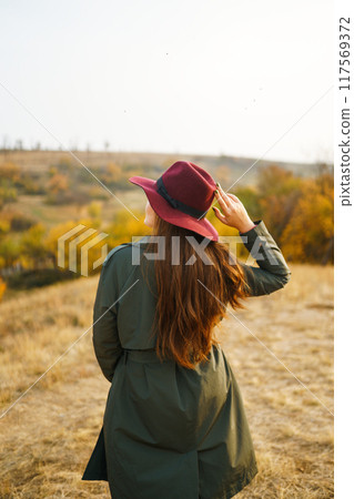 Beautiful stylish girl walks in the autumn park. The girl is dressed in a green coat and a red hat. 117569372