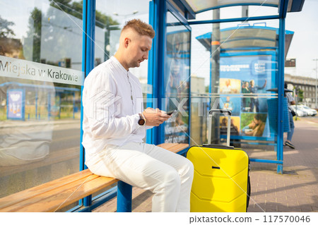 Handsome Tourist Caucasian business man traveler with bag and suitcase sit at public transport bus station waiting with mobile smart phone Handsome Tourist Caucasian business man traveler with bag and suitcase sit at public transport bus station waiting with mobile smart phone 117570046