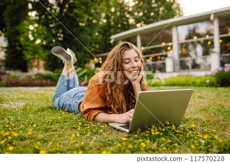Portrait of young beautiful female freelancer sitting on green meadow with laptop. Education online. Portrait of young beautiful female freelancer sitting on green meadow with laptop. Education online. 117570228