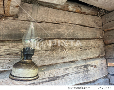 A kerosene lamp hangs on the wall of an old log shed. A kerosene lamp hangs on the wall of an old log shed. 117570438