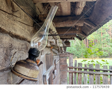 A kerosene lamp hangs on the wall of an old log shed. A kerosene lamp hangs on the wall of an old log shed. 117570439