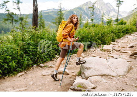 Stylish tourist woman with yellow backpack against backdrop of mountain scenery. Concept of travel. Stylish tourist woman with yellow backpack against backdrop of mountain scenery. Concept of travel. 117571233