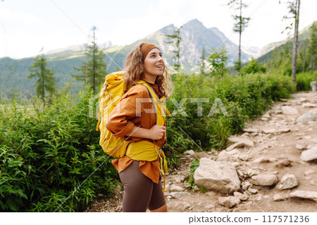 Young female traveler with hiking poles, bright backpack enjoys mountain scenery. Active lifestyle. Young female traveler with hiking poles, bright backpack enjoys mountain scenery. Active lifestyle. 117571236