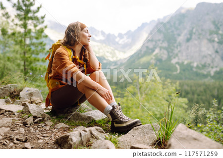 Hiking boot. Close-up of female legs in hiking boots on hiking trail, on top of mountain outdoors. 117571259