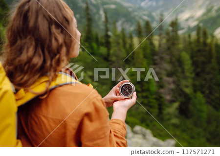 Wanderlust concept. Stylish woman holding a compass in her hand while traveling in the mountains. 117571271