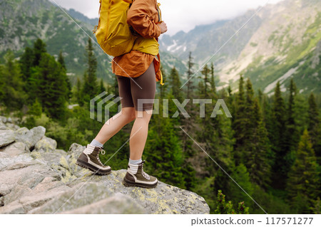 Hiking boot. Close-up of female legs in hiking boots on hiking trail, on top of mountain outdoors. 117571277