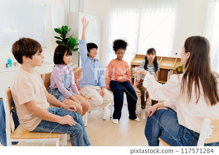 Multicultural primary school children participate in engaging group lesson. Teacher facilitates active learning through circular seating arrangement, encouraging student involvement and communication 117571284