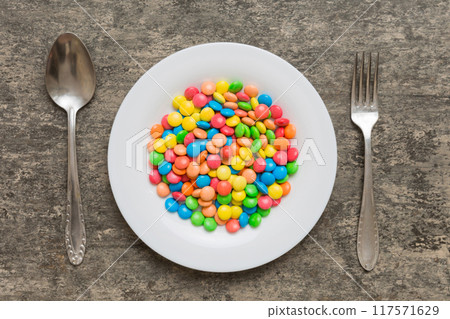 cutlery on table and sweet plate of candy. Health and obesity concept, top view on colored background cutlery on table and sweet plate of candy. Health and obesity concept, top view on colored background 117571629