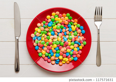 cutlery on table and sweet plate of candy. Health and obesity concept, top view on colored background cutlery on table and sweet plate of candy. Health and obesity concept, top view on colored background 117571631