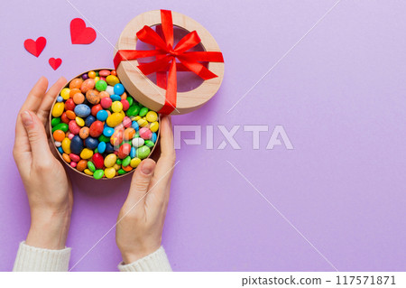Female hands with delicious candies in box on color background 117571871