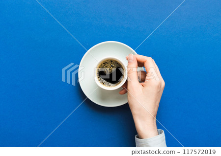 Minimalistic style woman hand holding a cup of coffee on Colored background. Flat lay, top view cappuccino cup. Empty place for text, copy space. Coffee addiction. Top view, flat lay Minimalistic style woman hand holding a cup of coffee on Colored background. Flat lay, top view cappuccino cup. Empty place for text, copy space. Coffee addiction. Top view, flat lay 117572019