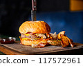 Burger with beef cutlet, a wheat bun and cheese, with a knife stuck into it, served with baked potatoes 117572961