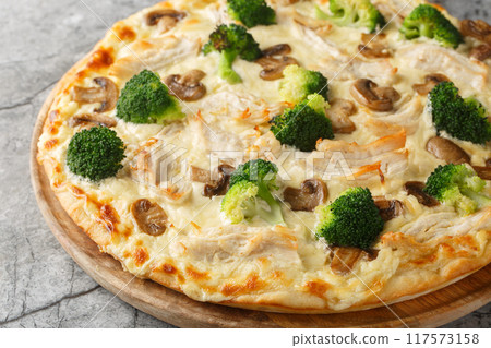 Italian white pizza with chicken, broccoli, mushrooms and cheese sauce close-up on wooden board. Horizontal Italian white pizza with chicken, broccoli, mushrooms and cheese sauce close-up on wooden board. Horizontal 117573158