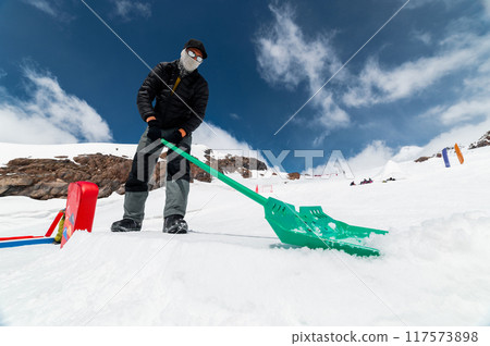Man clears snow at a ski resort in winter. A snow park worker shapes and prepares figures for skiing Man clears snow at a ski resort in winter. A snow park worker shapes and prepares figures for skiing 117573898