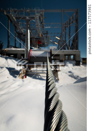A cable car station under construction high in the mountains in winter. Focus on a close-up of a thick cable car cable covered with snow 117573981