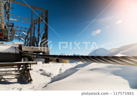 cable car towers, in the blue sky against the backdrop of snow-capped mountains. cable car construction, tourist resort 117573983