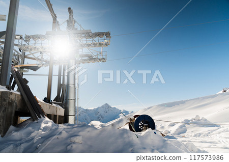 cable car towers, in the blue sky against the backdrop of snow-capped mountains. cable car construction, tourist resort cable car towers, in the blue sky against the backdrop of snow-capped mountains. cable car construction, tourist resort 117573986